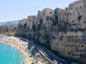 Spiaggia di Tropea con acque cristalline e il profilo delle scogliere, cipolla rossa in primo piano.